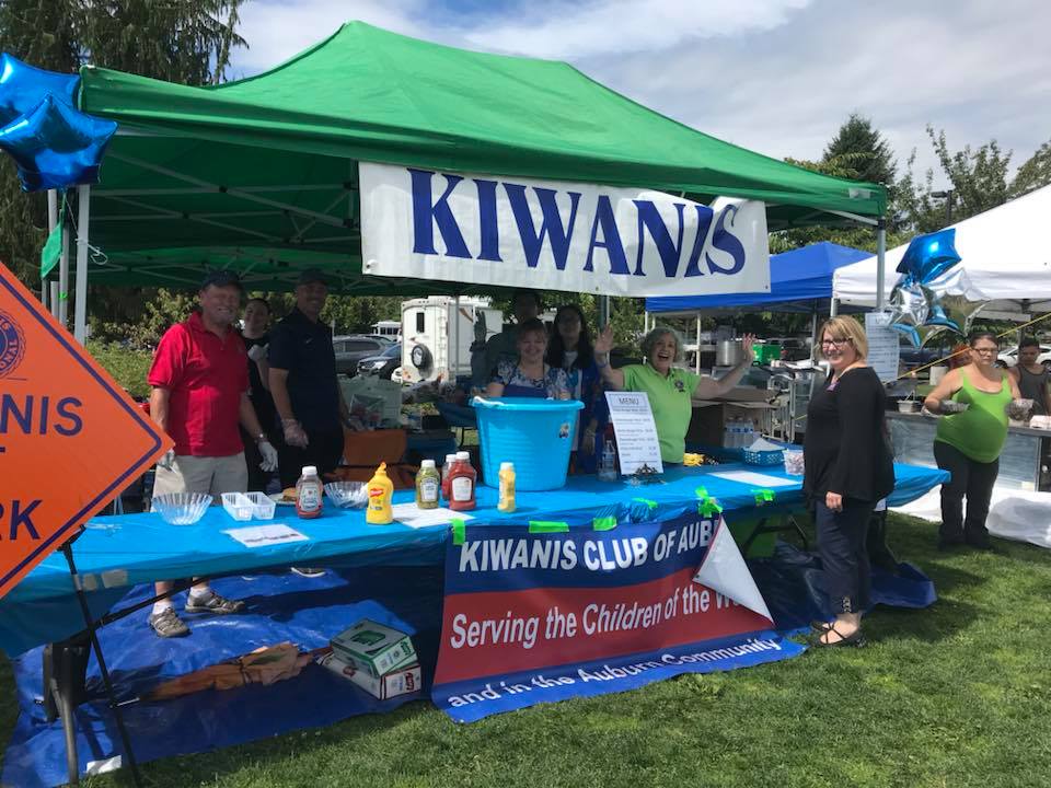 Kiwanis volunteers serve food from a tent at a summer community event. 